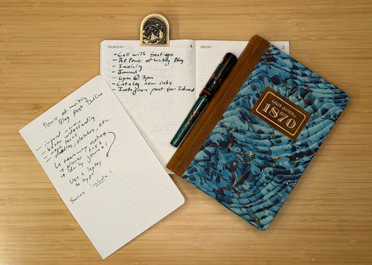 A picture showing a workflow ecosystem containing a tear-out page with notes for this blog post, a planner with this blog post as a to-do item, and a journaling notebook